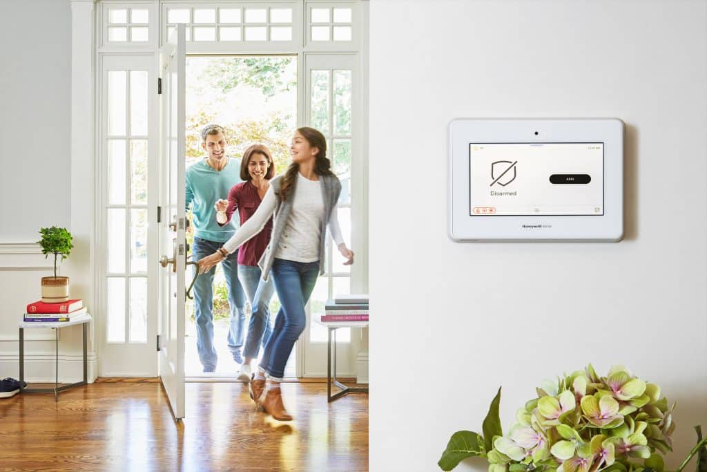 Happy teenager and parents entering bright home with smart home security panel on the wall.